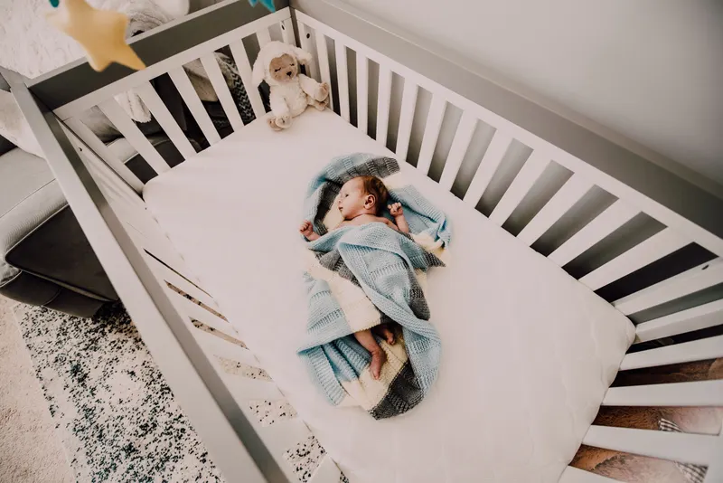 Babybett mit fester Matratze in einem aufgeräumten Kinderzimmer