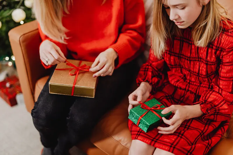 Familie packt Weihnachtsgeschenke gemeinsam im Wohnzimmer aus