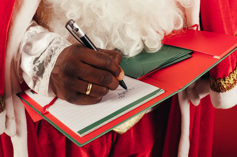 Person notiert Weihnachtswünsche in einem Notizbuch am Küchentisch